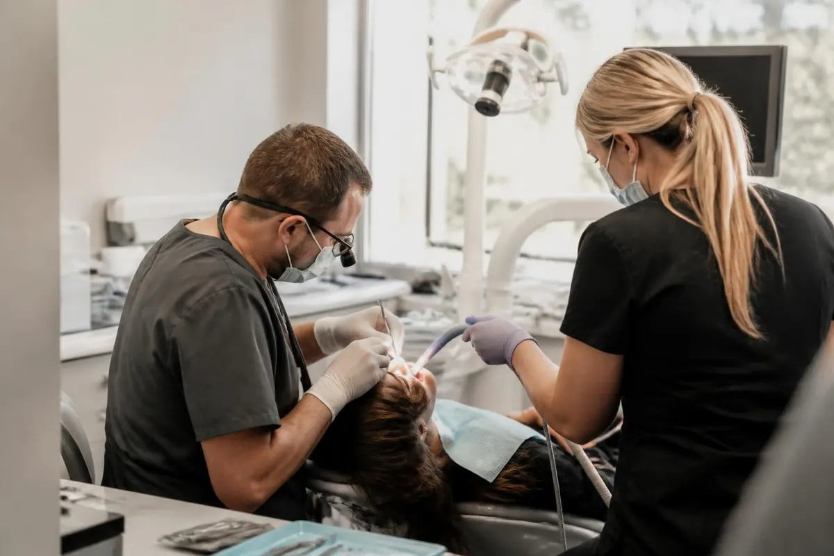 Dentist and assistant working on a patient in a daylit dental operatory. Illustrative image.